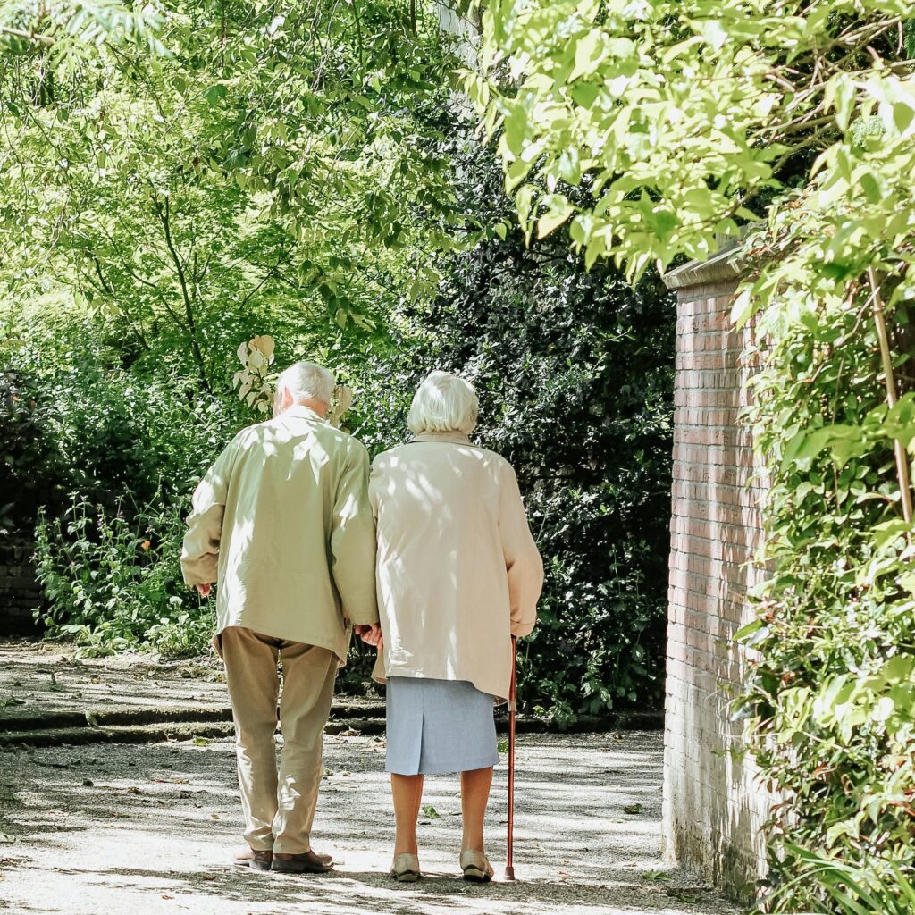 Casal de idosos caminhando juntos por um caminho cercado de vegetação.